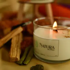 Płonąca świeca Natura od Pauli, z widocznym efektem tunelowania świecy, otoczona patyczkami palo santo i suszonymi liśćmi.