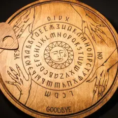 Drewniana plansza Ouija z literami, cyframi i symbolem słońca. Czy to sposób, jak wywołać ducha bez świeczek?