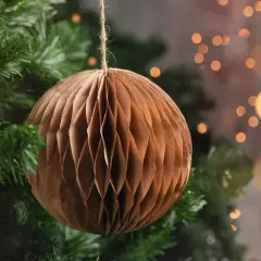 Brązowa, papierowa ozdoba choinkowa w kształcie kuli wisi na gałęzi choinki.