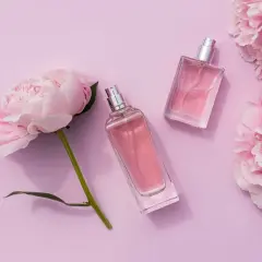 Dwa eleganckie flakony perfum i pąki piwonii na pastelowym tle. Zapach piwonii unosi się w powietrzu.