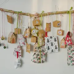 Ręcznie robiony kalendarz adwentowy dla mężczyzn diy wisi na gałęzi. Małe paczuszki i ozdoby świąteczne z numerami.