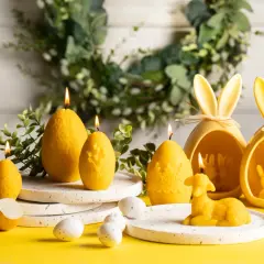 Wielkanocne rodzaje świeczek: jajka, baranek i zajączki w żółtych ceramicznych koszyczkach.
