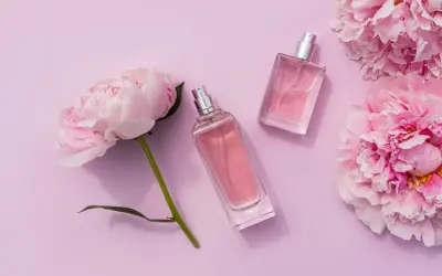 Dwa eleganckie flakony perfum i pąki piwonii na pastelowym tle. Zapach piwonii unosi się w powietrzu.