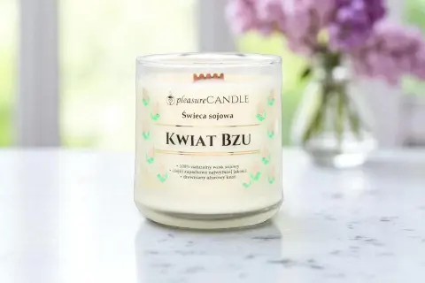 Szklana świeca zapachowa "Kwiat Bzu" z drewnianym knotem, na tle rozmytych kwiatów bzu.