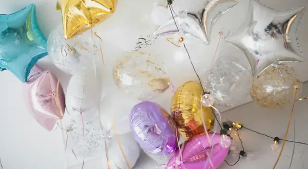 Kolorowe balony do helu w kształcie gwiazdek i okrągłe z konfetti, tworzą radosną dekorację.