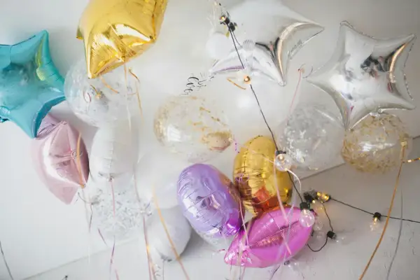 Kolorowe balony do helu w kształcie gwiazdek i okrągłe z konfetti, tworzą radosną dekorację.