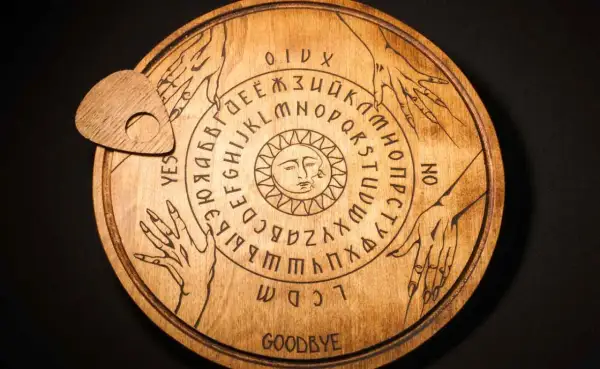 Drewniana plansza Ouija z literami, cyframi i symbolem słońca. Czy to sposób, jak wywołać ducha bez świeczek?